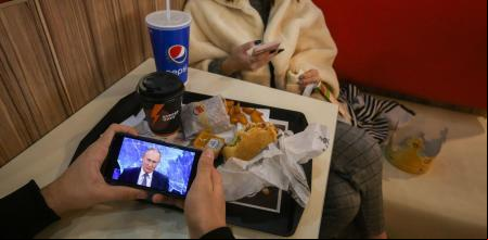 Dos jóvenes siguen en directo un discurso de Putin en un restaurante de comida rápida en Moscú en el año 2020
